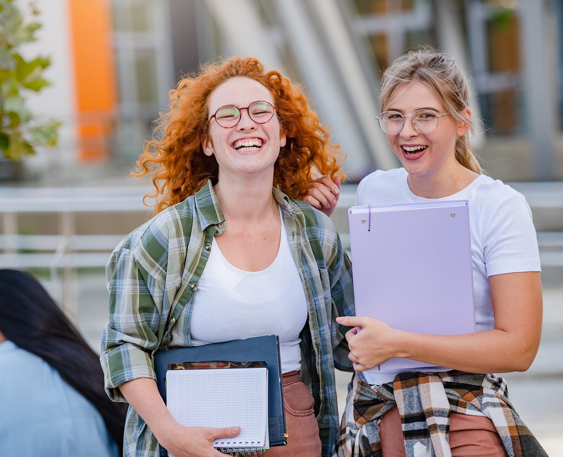 Due studentesse sorridenti con quaderni e cartelline